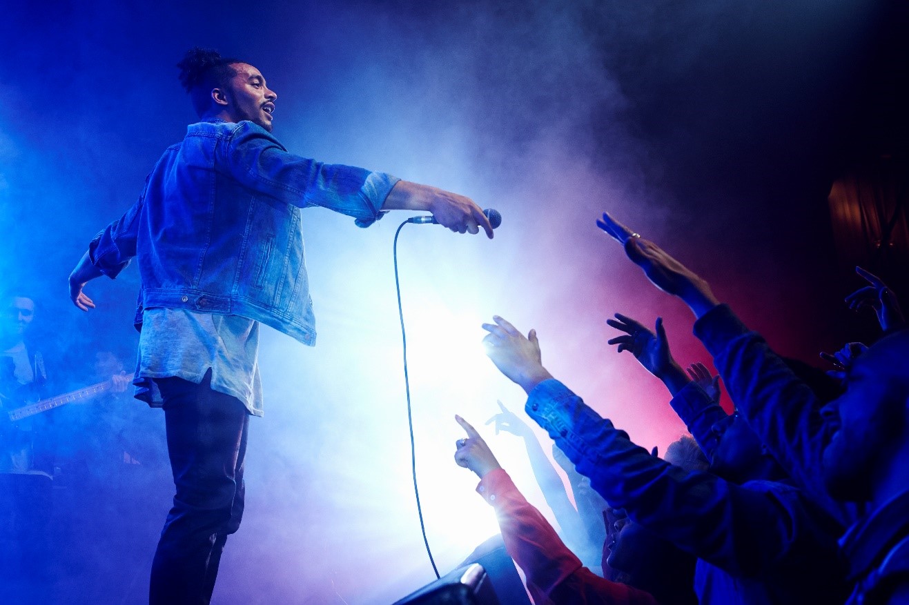 A person holding a microphone and pointing at a crowd

Description automatically generated